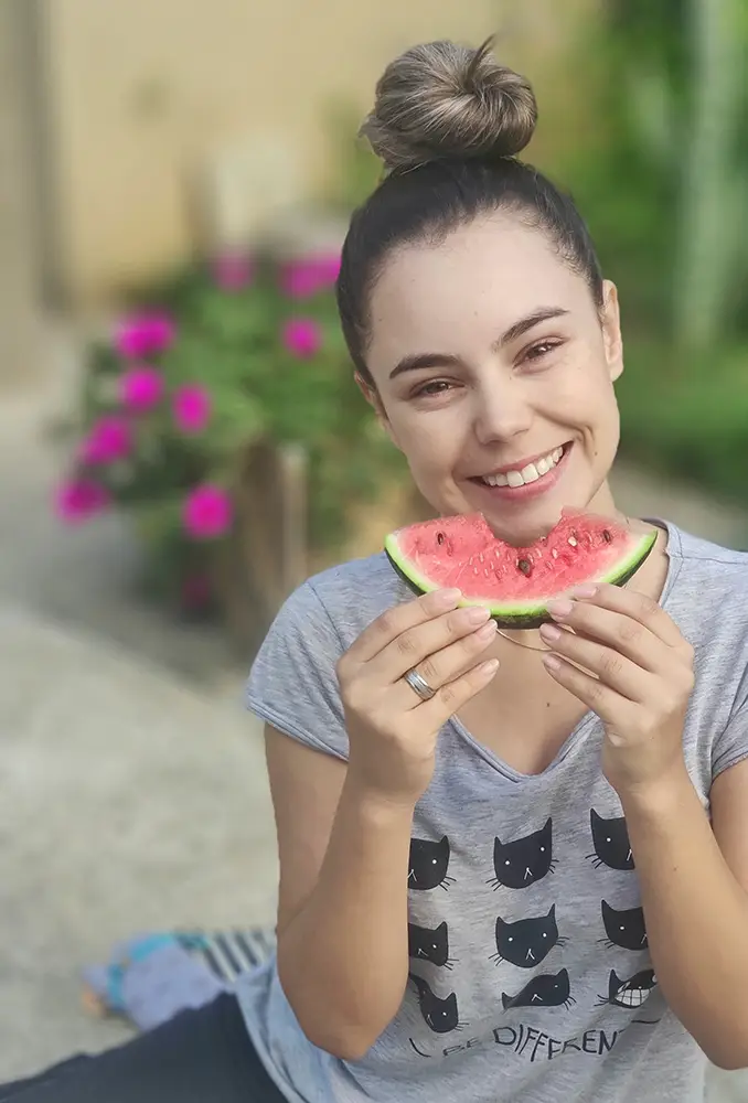 Orthodontic patient holding a slice of watermelon in front of her face as if it's a smile because she knows there are certain foods to avoid when wearing braces